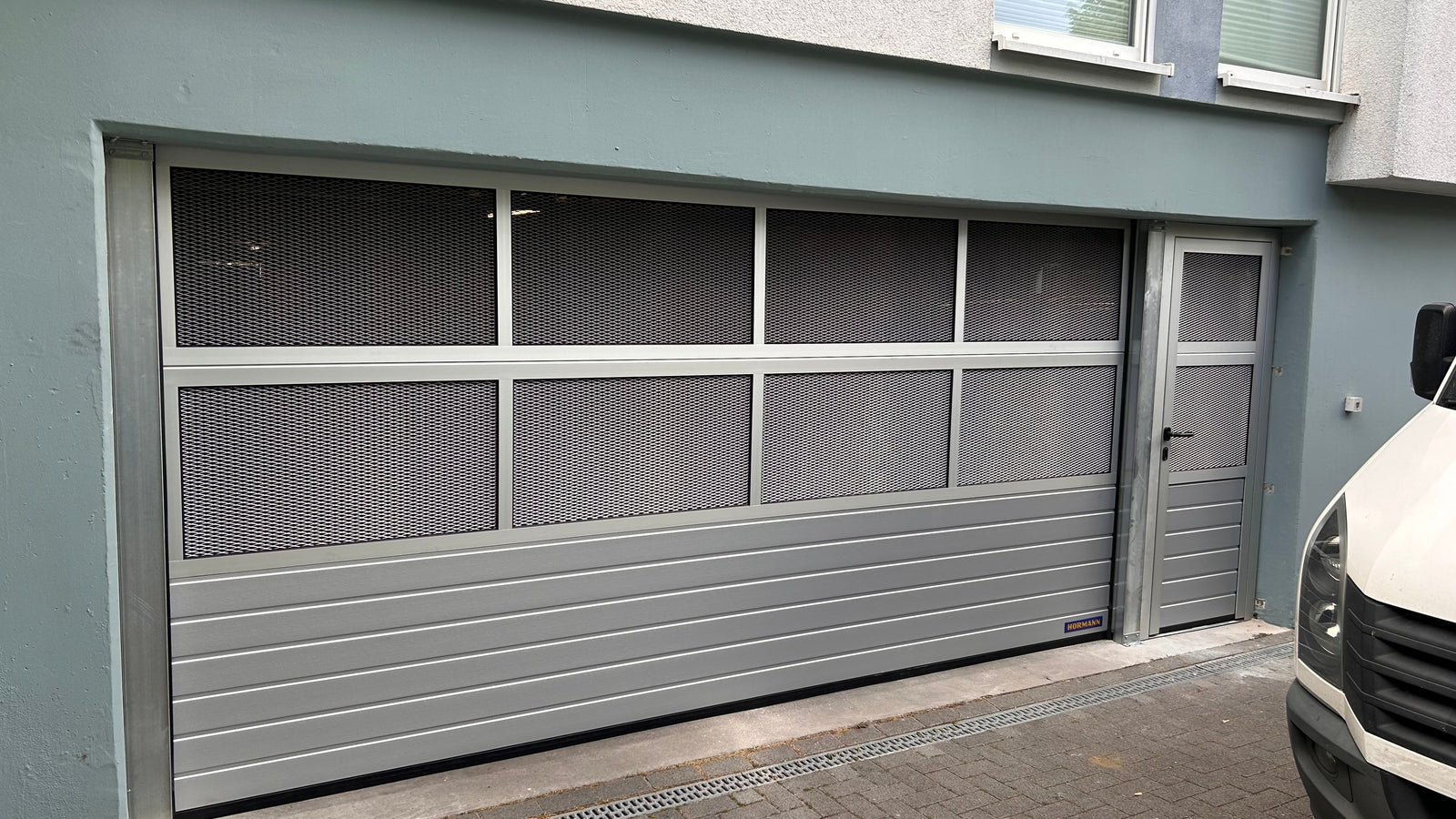 Tormeister24 Hörmann Fachhändler Techniker prüft ein geöffnetes Tiefgaragentor in einer Wohnanlage, gelb‑anthrazite Optik