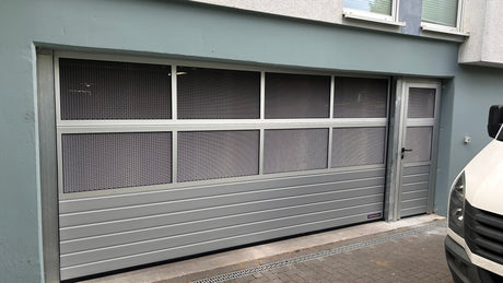 Tormeister24 Hörmann Fachhändler Techniker prüft ein geöffnetes Tiefgaragentor in einer Wohnanlage, gelb‑anthrazite Optik